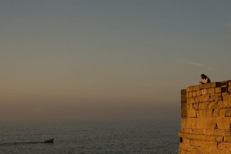 Woman relaxing, reading and watching sunset over the sea from the ramparts at Essaouira, Morocco