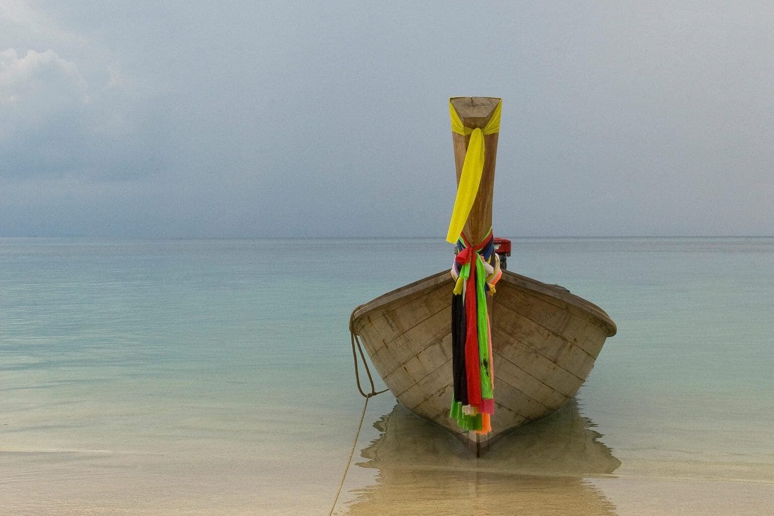A moored Longtail Boat with colourful pieces of silk cloth tied to the bowsprit at Phi Phi beach, Thailand