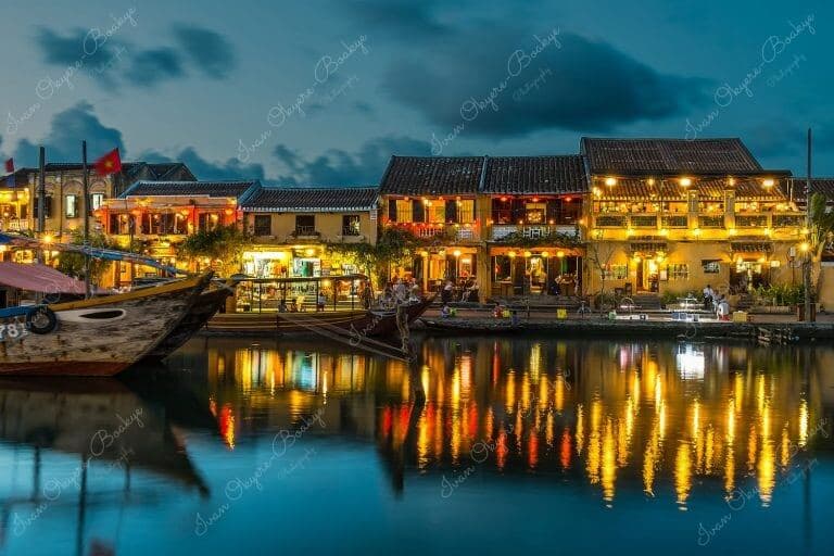 A beautiful evening view of fishing boat restaurants and illuminated yellow pastel coloured restaurant buildings reflecting in the Thu Bon River at Hoi Ann Old Town riverfront, Vietnam