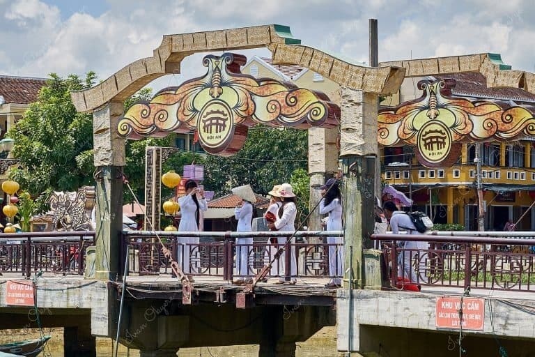 Group of Vietnamese women wearing traditional Ao Dai taking photographs on the Bridge of Lights (Cau An Hoi) in Hoi An, Vietnam