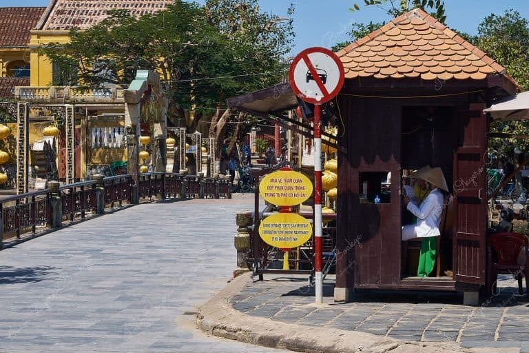 Nguyen Phuc Chu view of the Bridge of Lights (Cau An Hoi) and staff wearing traditional clothing and non la hats in ticket booth in Hoi An, Vietnam
