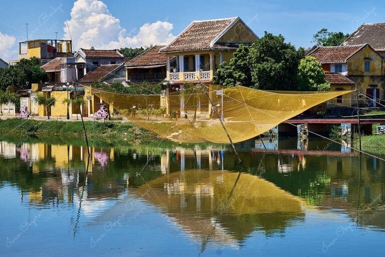 Large yellow fishing net suspended above the Thu Bon River and yellow pastel coloured houses in the background at Hoi Ann Old Town riverfront, Vietnam