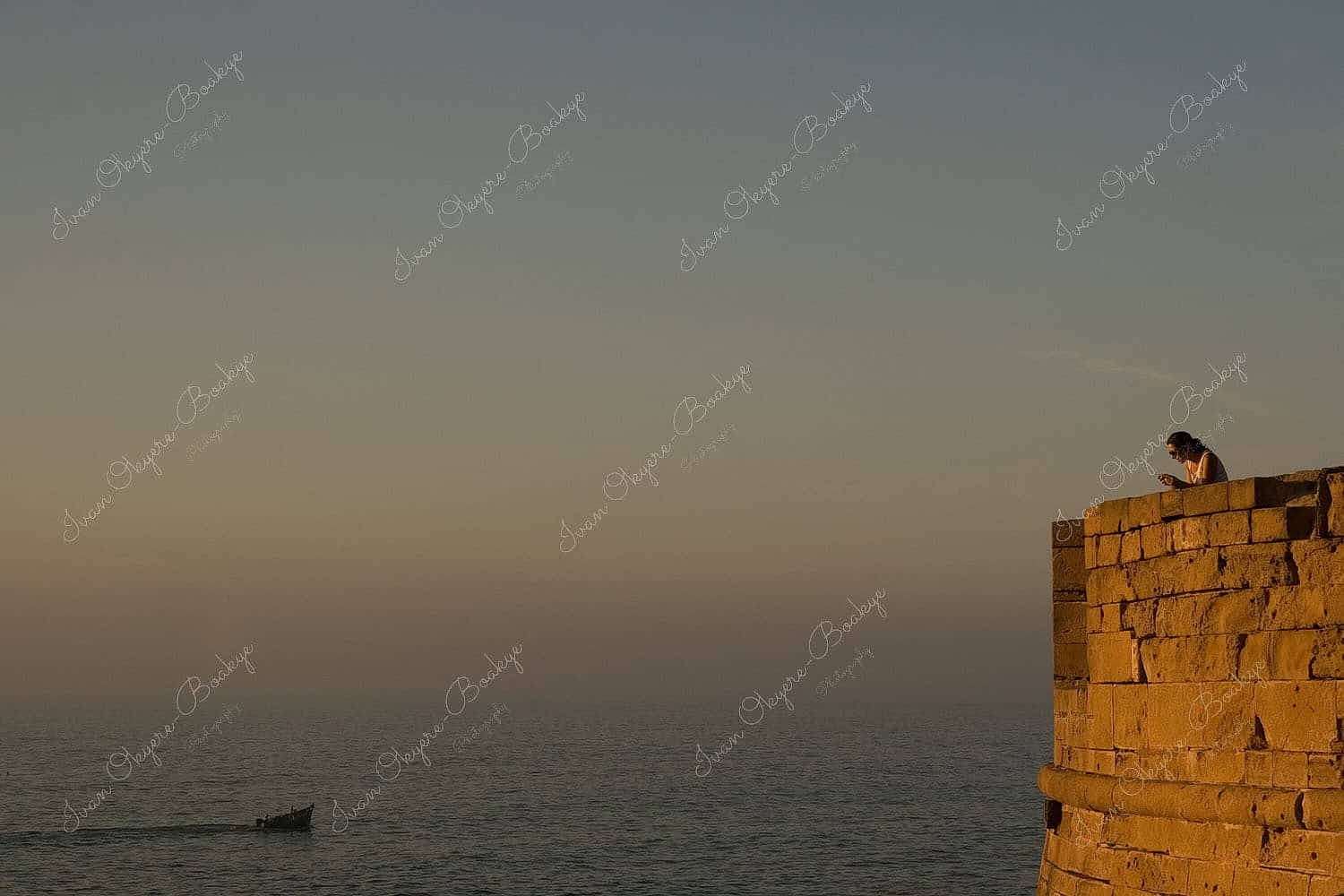 Woman relaxing, reading and watching sunset over the sea from the ramparts at Essaouira, Morocco