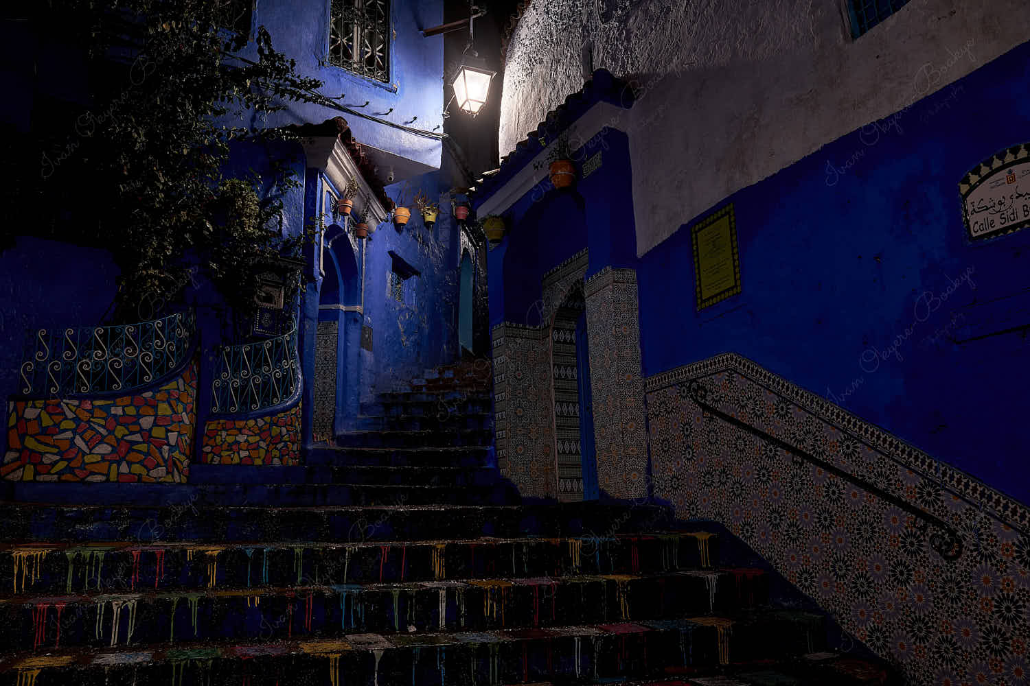 Illuminated steps and colorful mosaic and blue walls in an empty Calle Sidi Buchuka side street at night in old town medina, Chefchaouen, Morocco