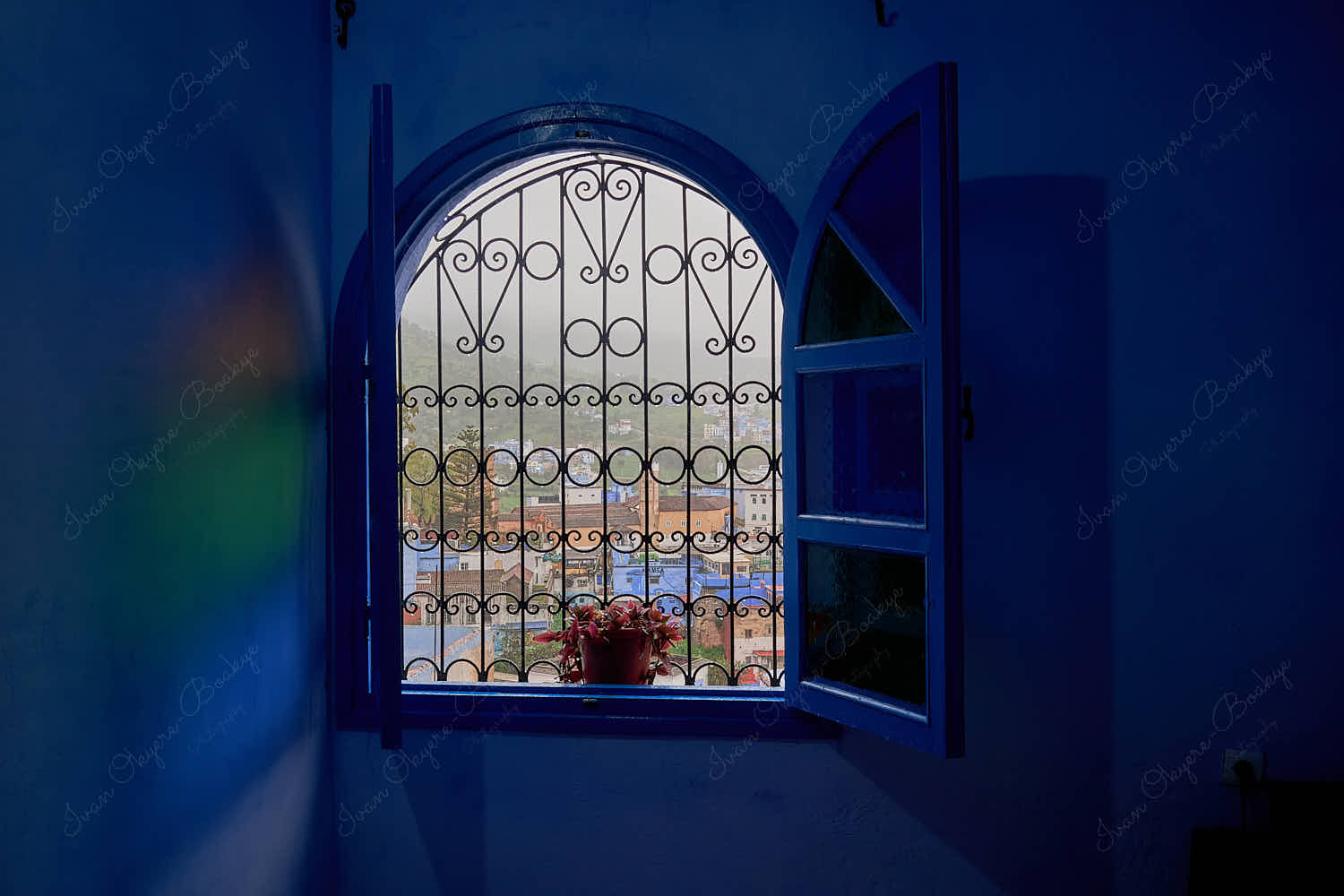 Framed rainy high angle window view through bars of Grand Mosque of Chefchaouen and Kasbah in old town medina, Chefchaouen, Morocco