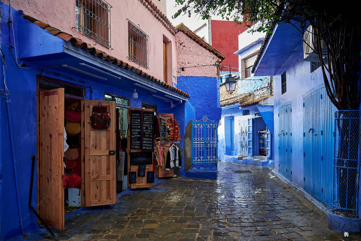 Leather bags and Moroccan clothes souvenirs shops in an empty street in the blue walled old town medina, Chefchaouen, Morocco