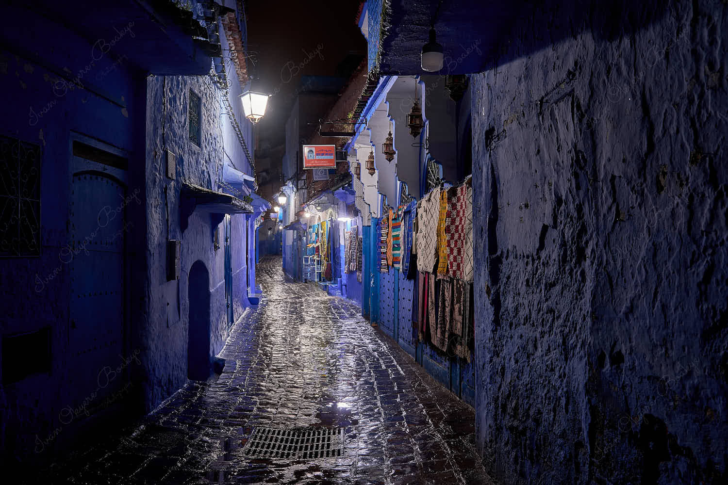 A nighttime view of an illuminated carpet shop in an empty street in the blue walled old town medina, Chefchaouen, Morocco