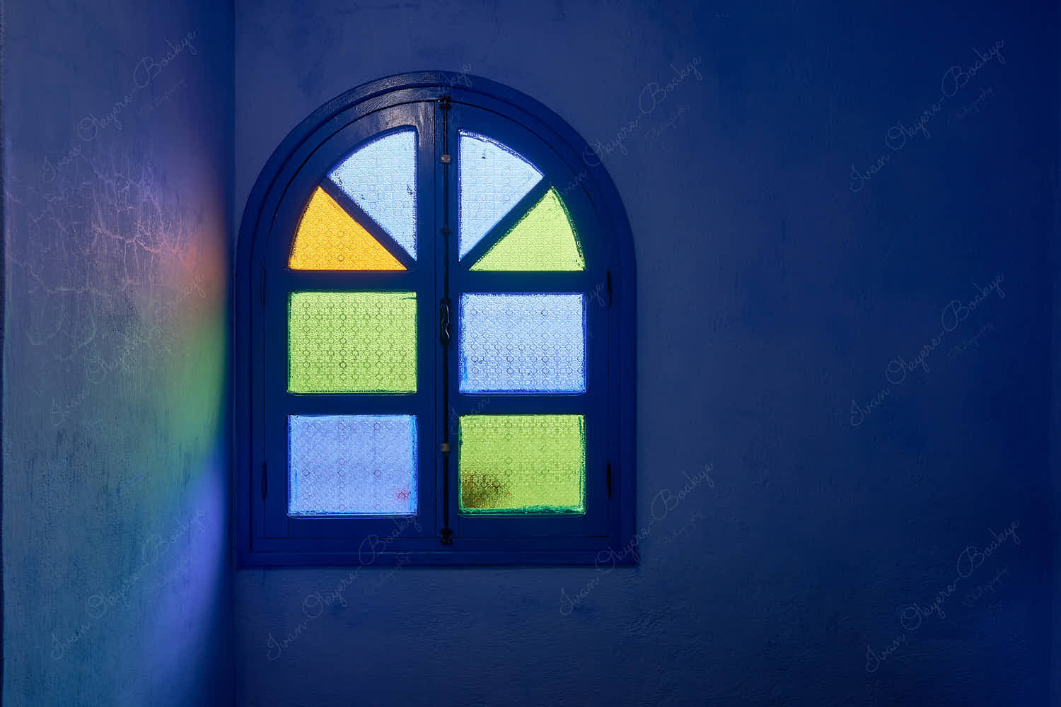 Indoor view of diffused natural light through green, blue and yellow glass stained panes in a closed arched wooden window, Chefchaouen, Morocco