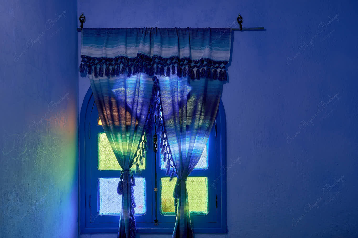 Diffused colors light coming through curtains framed green, blue and yellow glass stained panes in closed arched wooden window, Chefchaouen, Morocco