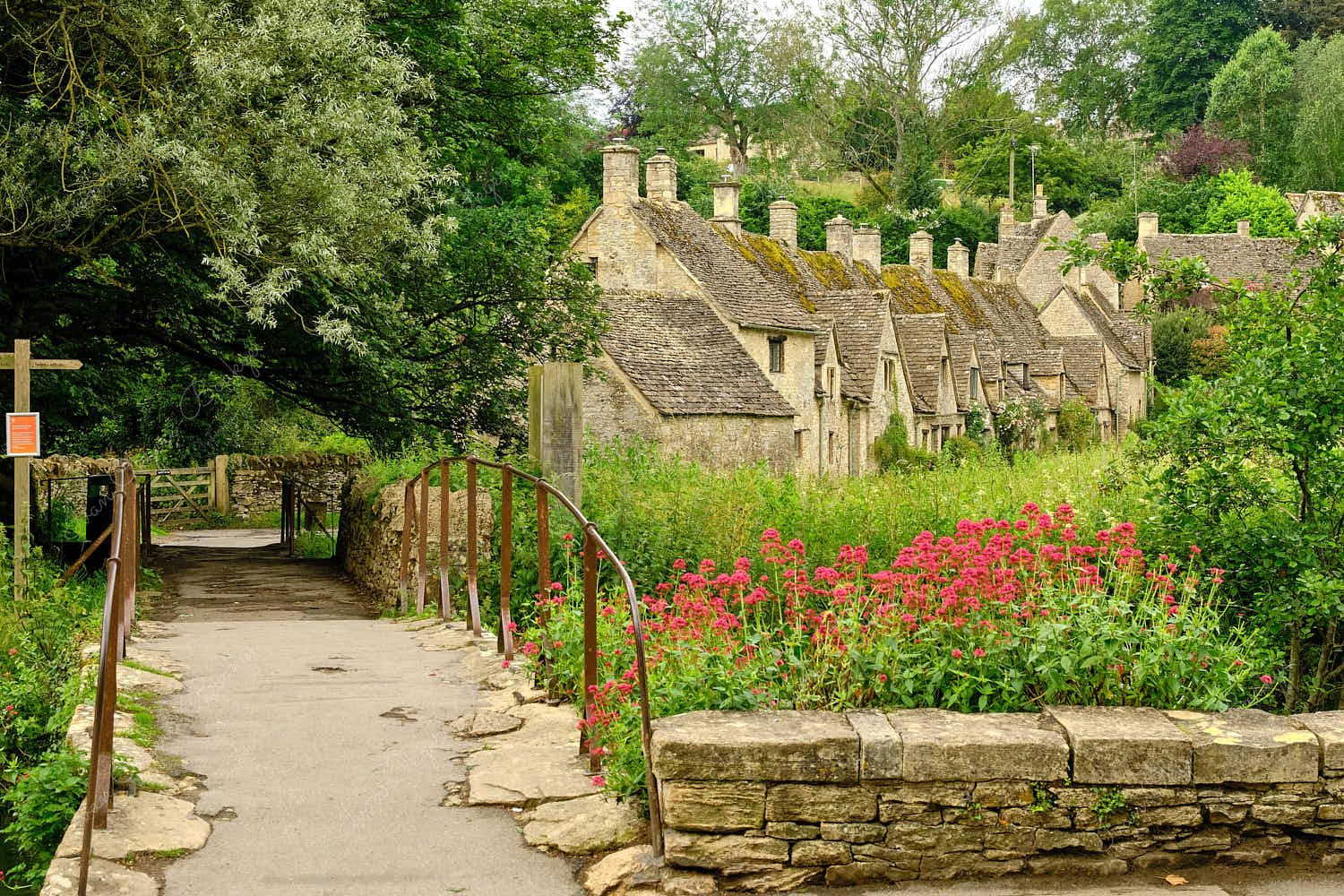 View of stone bridge footpath towards the picturesque Arlington Row Weavers Cottages, Bibury, Cotswolds, England, UK