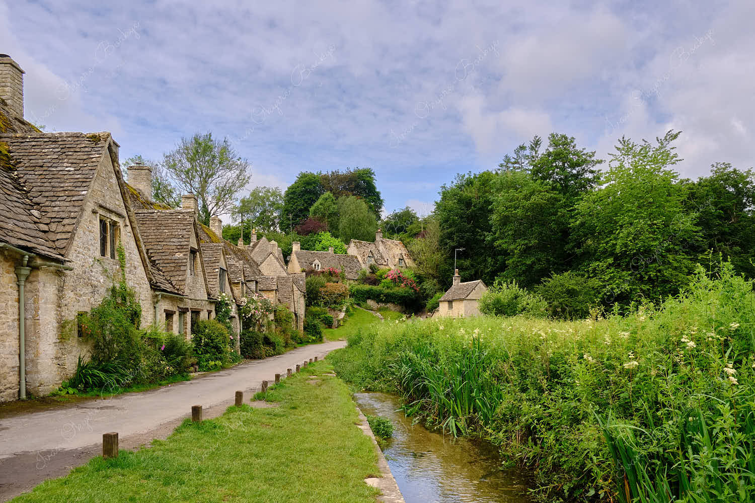 View of footpath and stream leading past the famous picturesque Arlington Row Weavers Cottages, Bibury, Cotswolds, England, UK