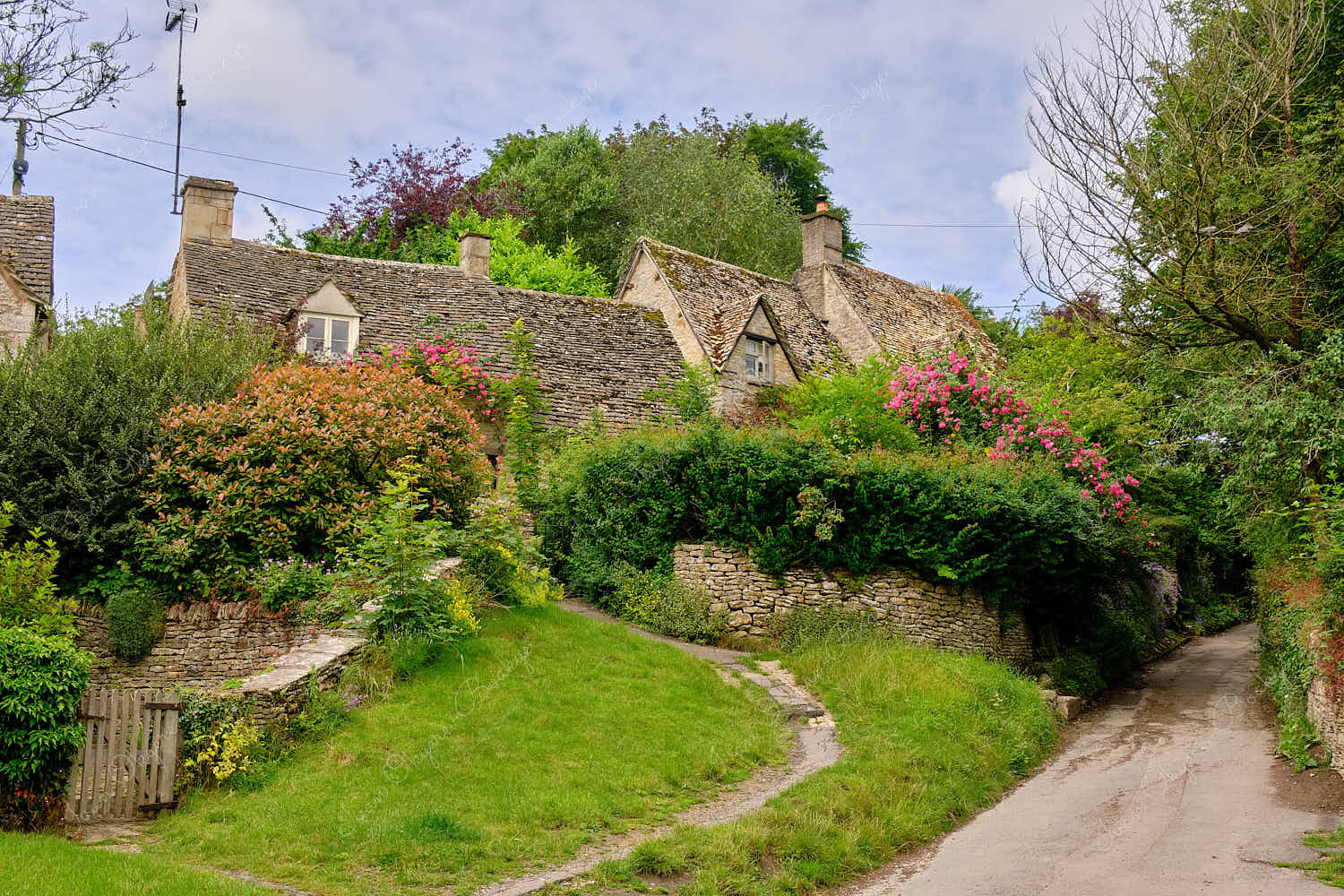 View from footpath of the famous picturesque Arlington Row Weavers Cottages and gardens, Bibury, Cotswolds, England, UK