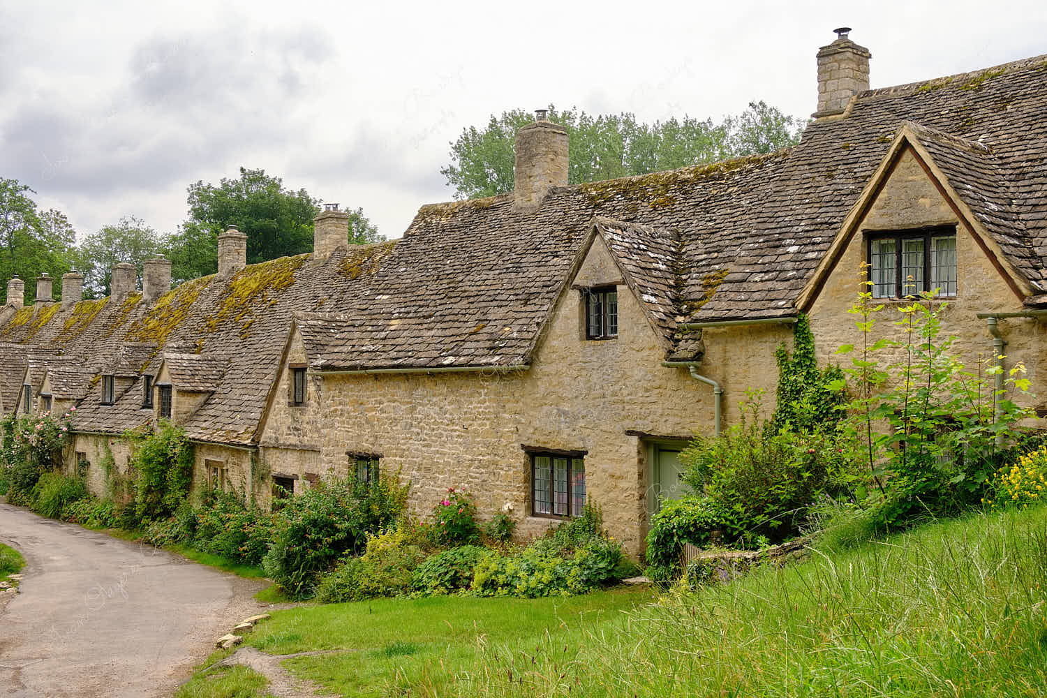 View from footpath leading past the famous picturesque Arlington Row Weavers Cottages, Bibury, Cotswolds, England, UK