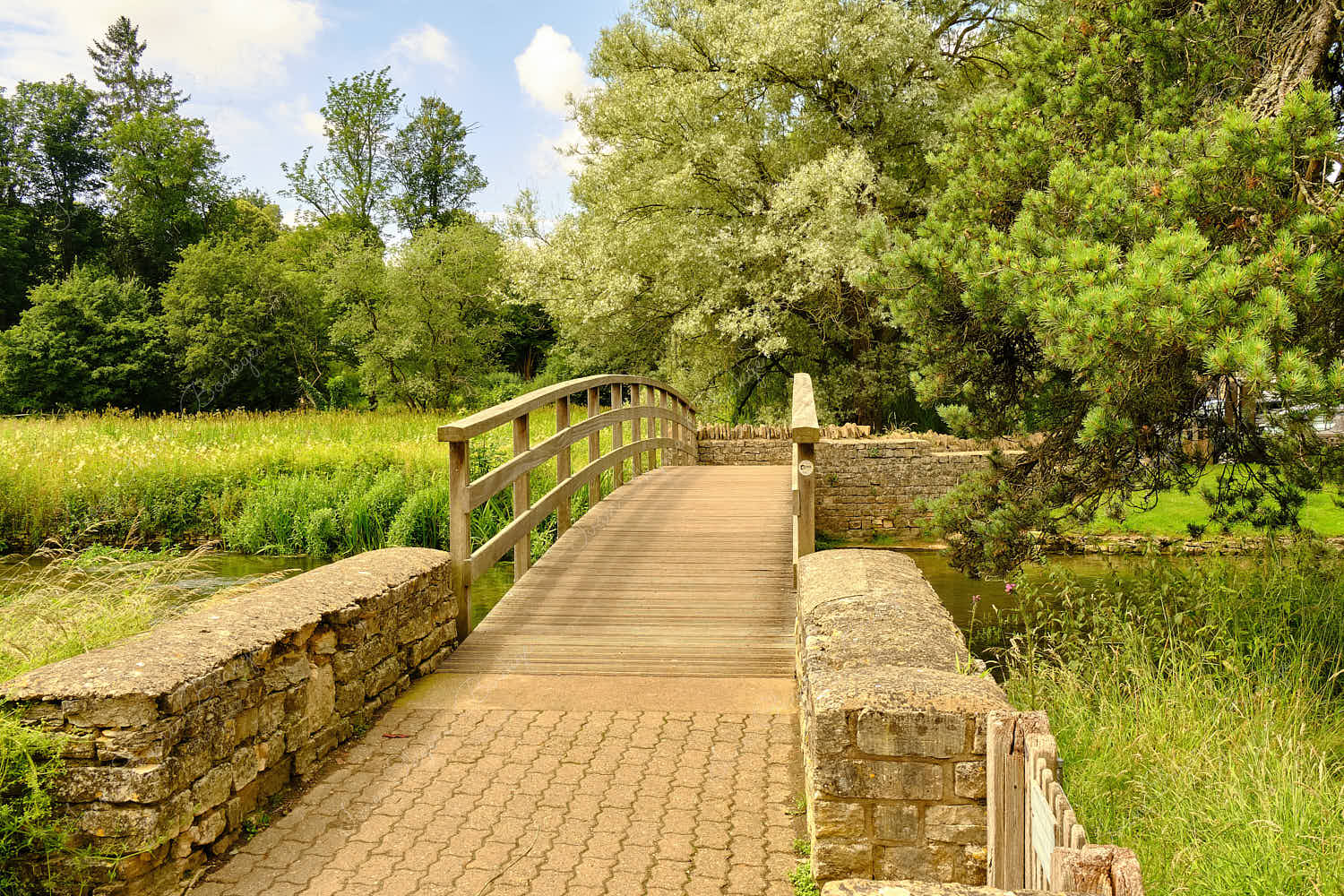 View of a wooden footbridge over the River Coln to the Rack Isle water meadow in the Cotswold village of Bibury, England, UK