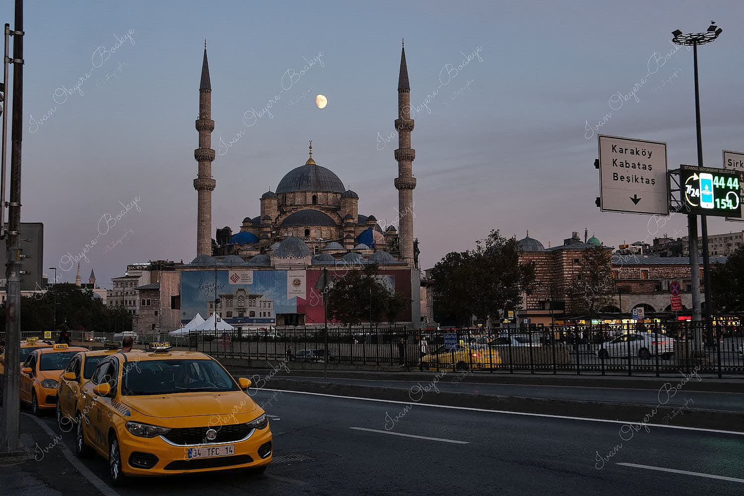 Moon between the minarets of the New Queen Mother Mosque with a queue of yellow taxis in the streets outside the mosque, Istanbul, Turkey