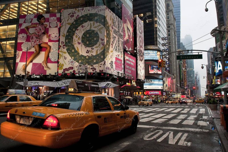 Yellow cabs in Times Square at night in front of large Liberty of London launch advertising billboards, New York, America