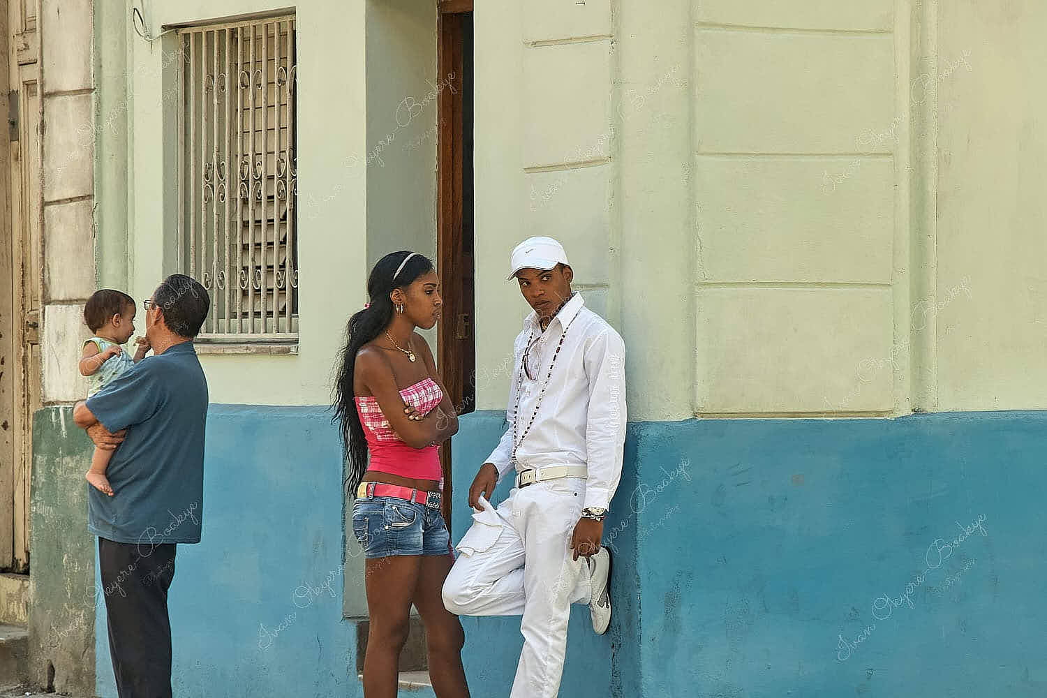 Young cuban man wearing all white Santeria traditional clothing leaning on wall in discussion with his girlfriend in Centro Havana, Cuba