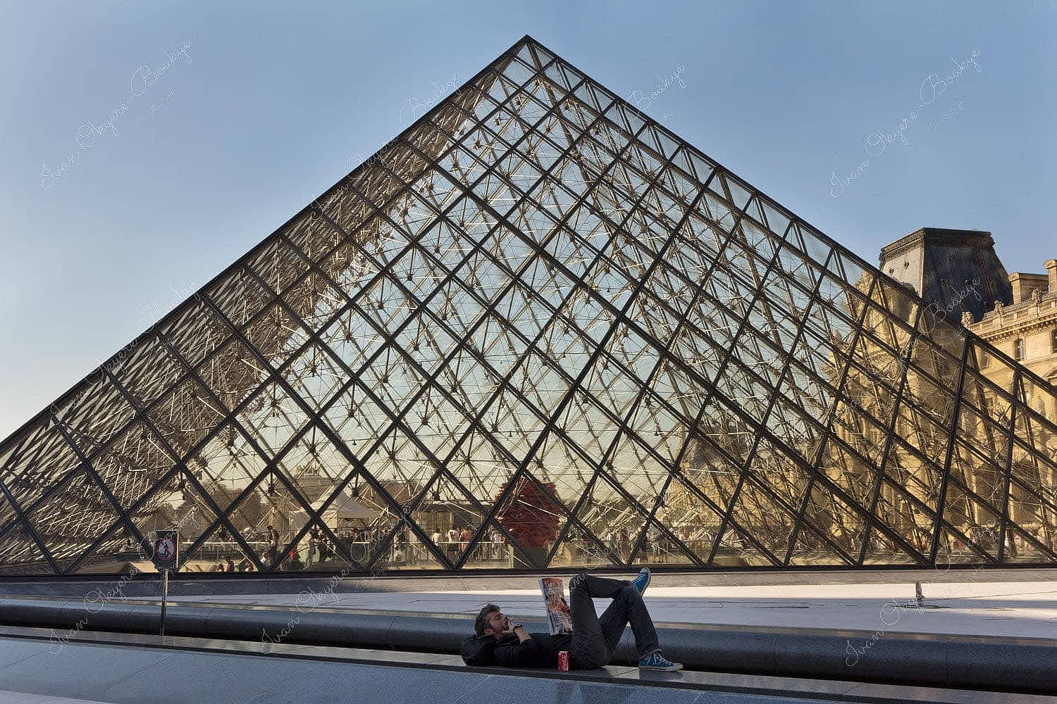 Man lying down in a quiet place behind the main Louvre Pyramid entrance at Musee du Louvre, Paris, France