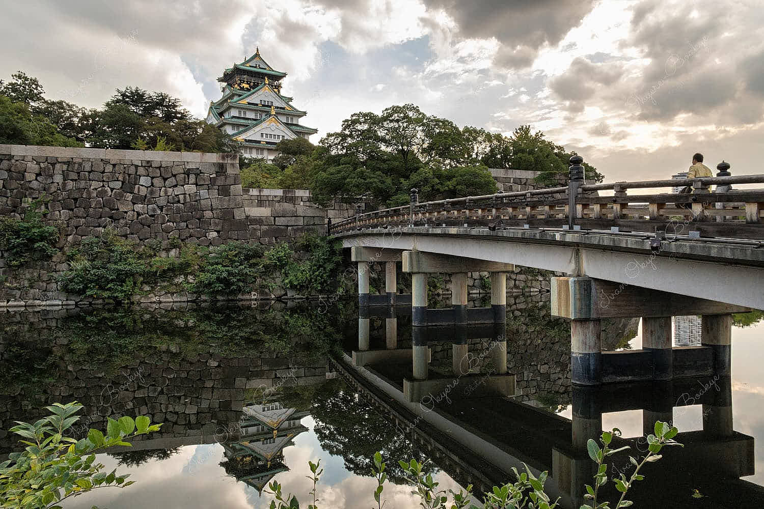 A moat bridge with castle reflections in the water leading up to the majestic Osaka Castle (Osakajo) in Osaka, Japan