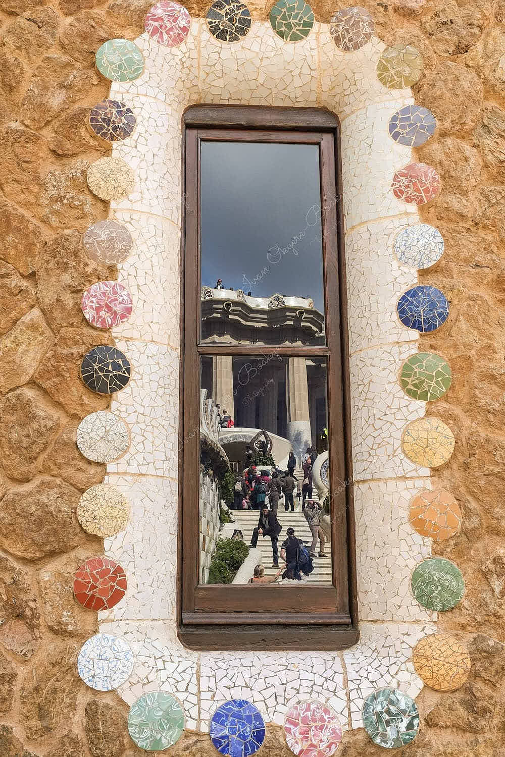 Reflection of the Dragon stairway and columns of the Hypostyle room in the window of Casa del Guarda in Park Güell, Barcelona, Spain