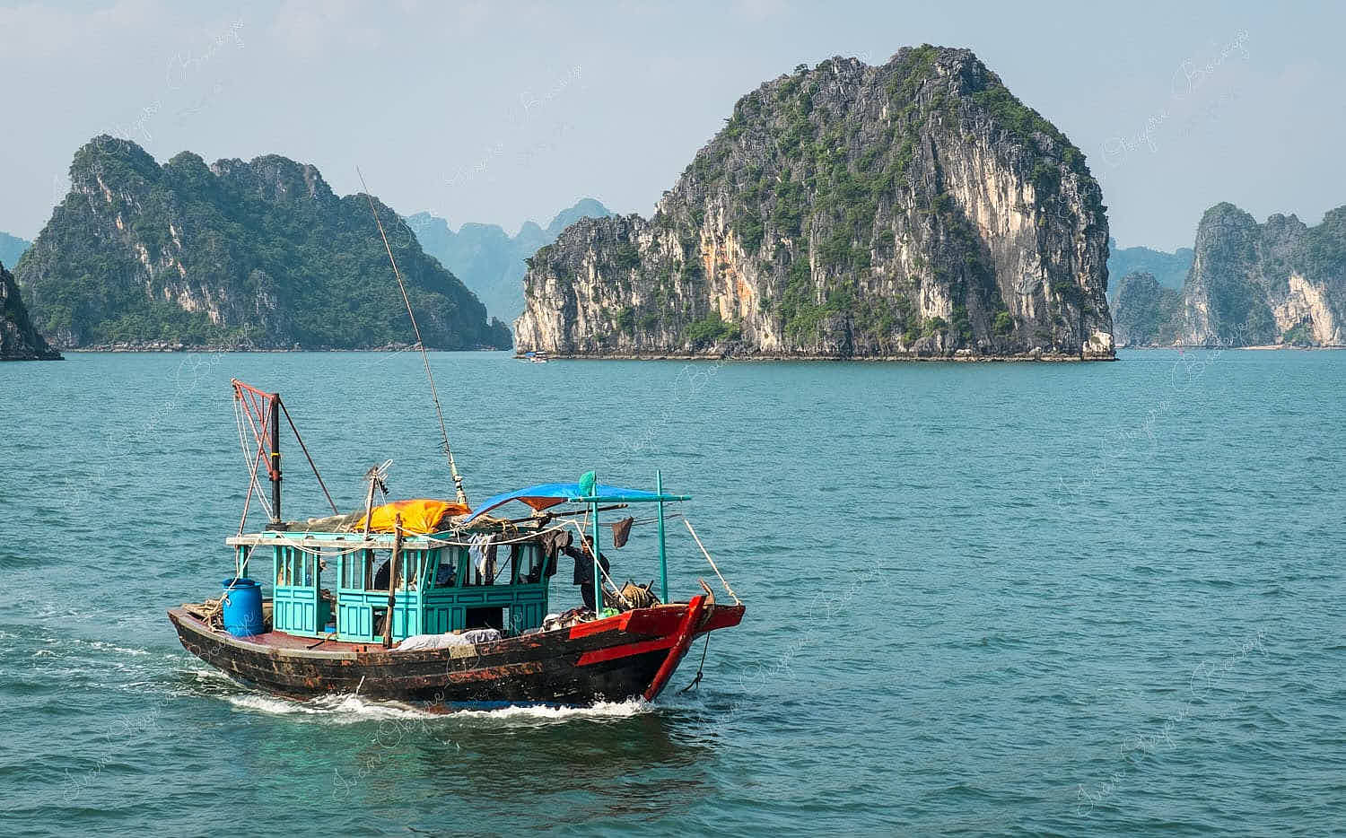 Fisherman standing on his fishing boat with karst mountains in the landscape background, Halong Bay, Vietnam