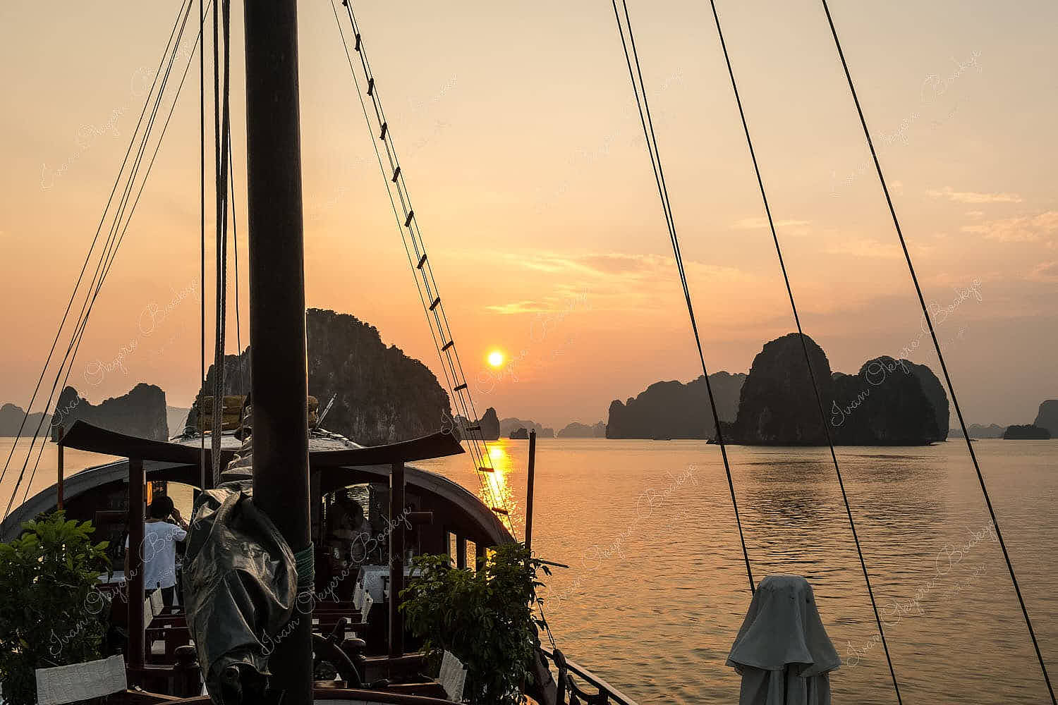 Junk boat sailing towards sunset surrounded by karst mountains in Halong Bay, Vietnam
