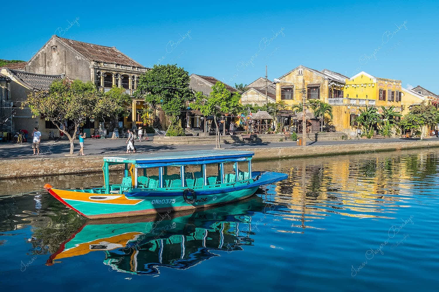 A gorgeous afternoon view of a multicoloured fishing boat and yellow pastel coloured buildings reflecting in the Thu Bon River at Hoi Ann Old Town riverfront, Vietnam