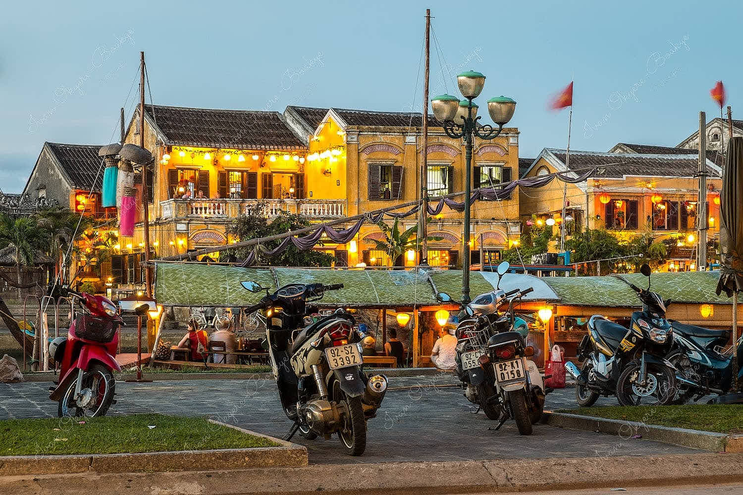 Moored fishing boat restaurant at Thu Bon River with illuminated yellow pastel coloured restaurant buildings at Hoi Ann Old Town riverfront, Vietnam
