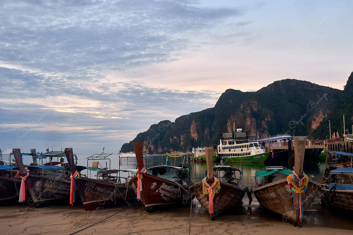 Moored longtail boats with tied pieces of coloured silk cloth on their bows at low tide on Tonsai Bay at dawn, Kho Phi Phi, Thailand