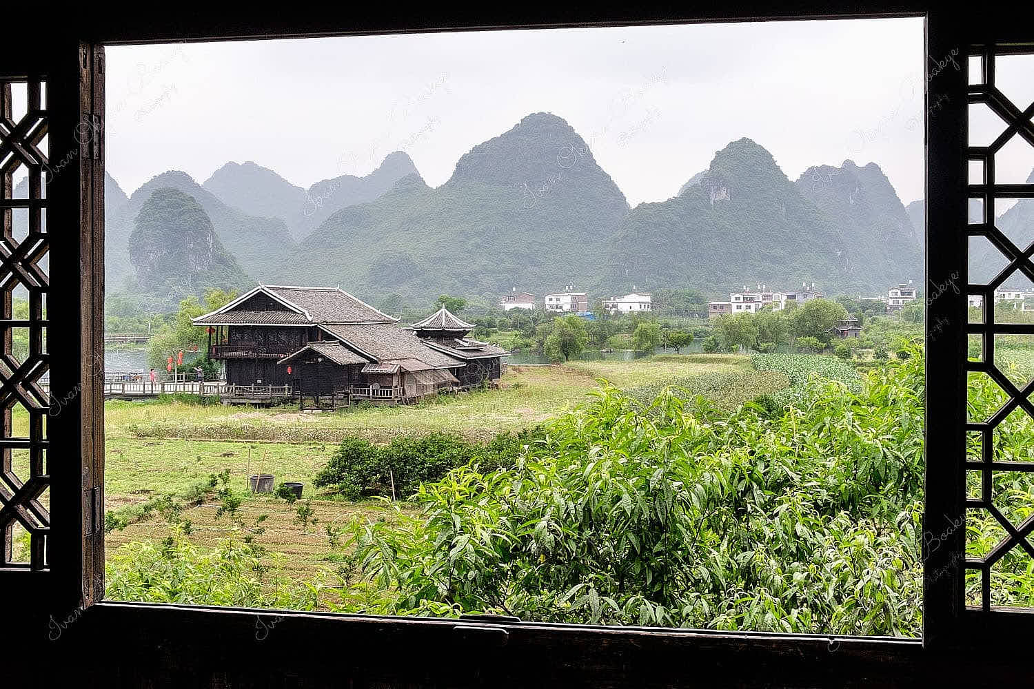 Window framed view of the lush green farmland, buildings and majestic karst mountains landscape of Shangri-la Park, Guilin, China