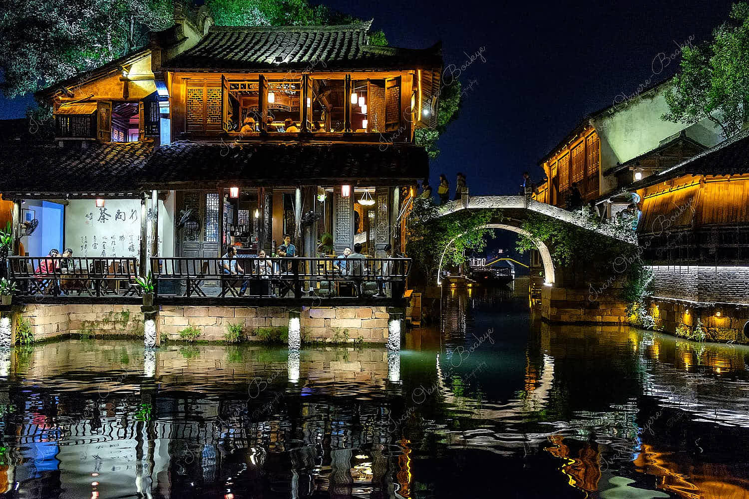 Night time view of people eating and socialising in a waterfront restaurant in Wuzhen West Scenic Zone water town, Zhejiang, China