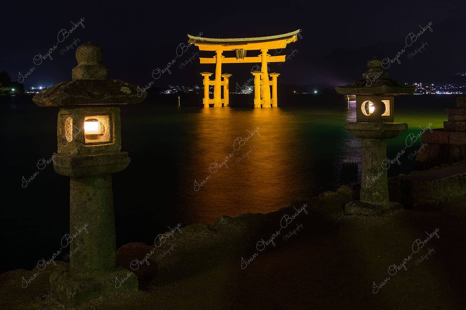 The famous Torii Gate at Miyajima Island illuminated at night with lit stone lanterns in the foreground, Miyajima, Japan