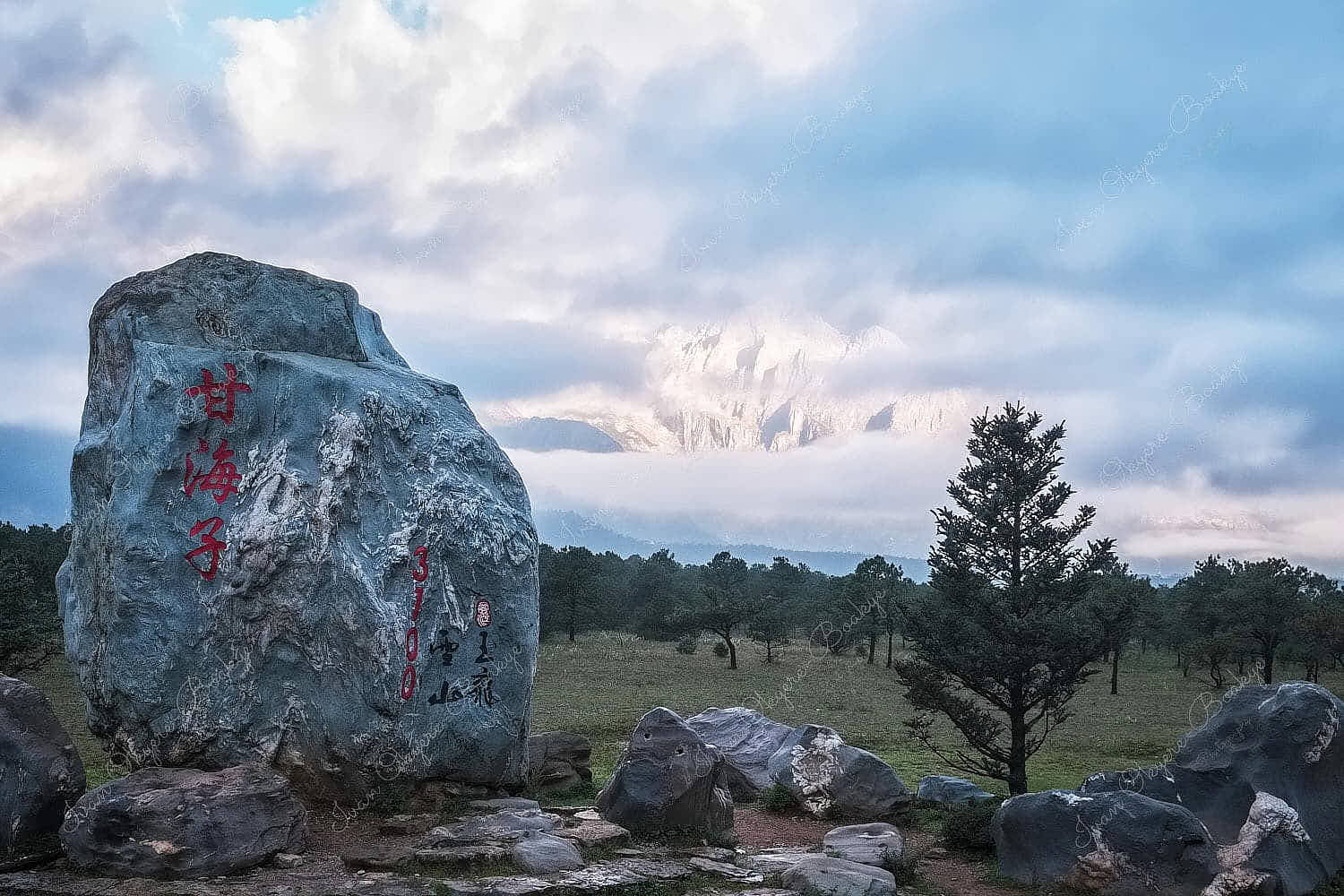 View of the snow covered Jade Dragon Snow Mountain peeking through the clouds at sunrise from the Dry Sea Meadow, Yunnan, China