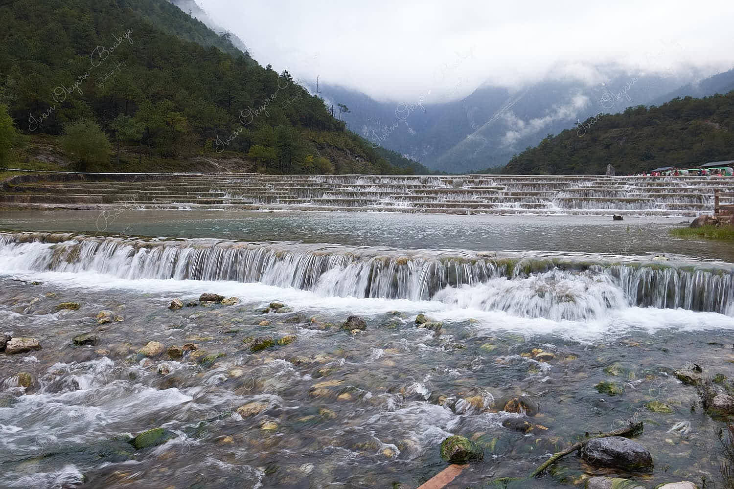 Cascading mini waterfalls of the Baishui River surrounded by the fog covered peaks of Jade Dragon Snow Mountain in Blue Moon Valley, Yunnan, China