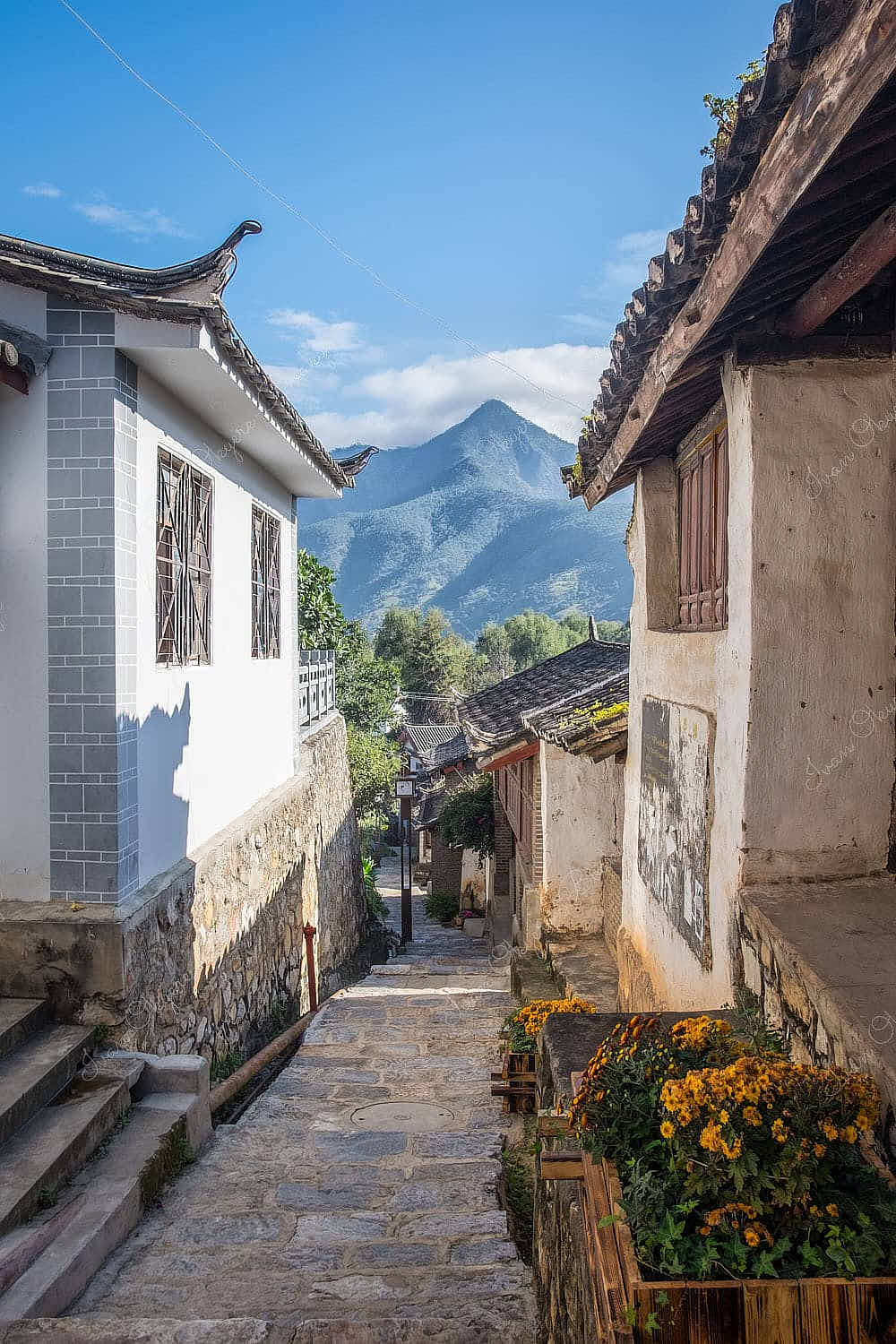 A side street view of traditional Chinese homes with mountains in the background in Stone Drum Town, Shanghri-La, Yunnan, China