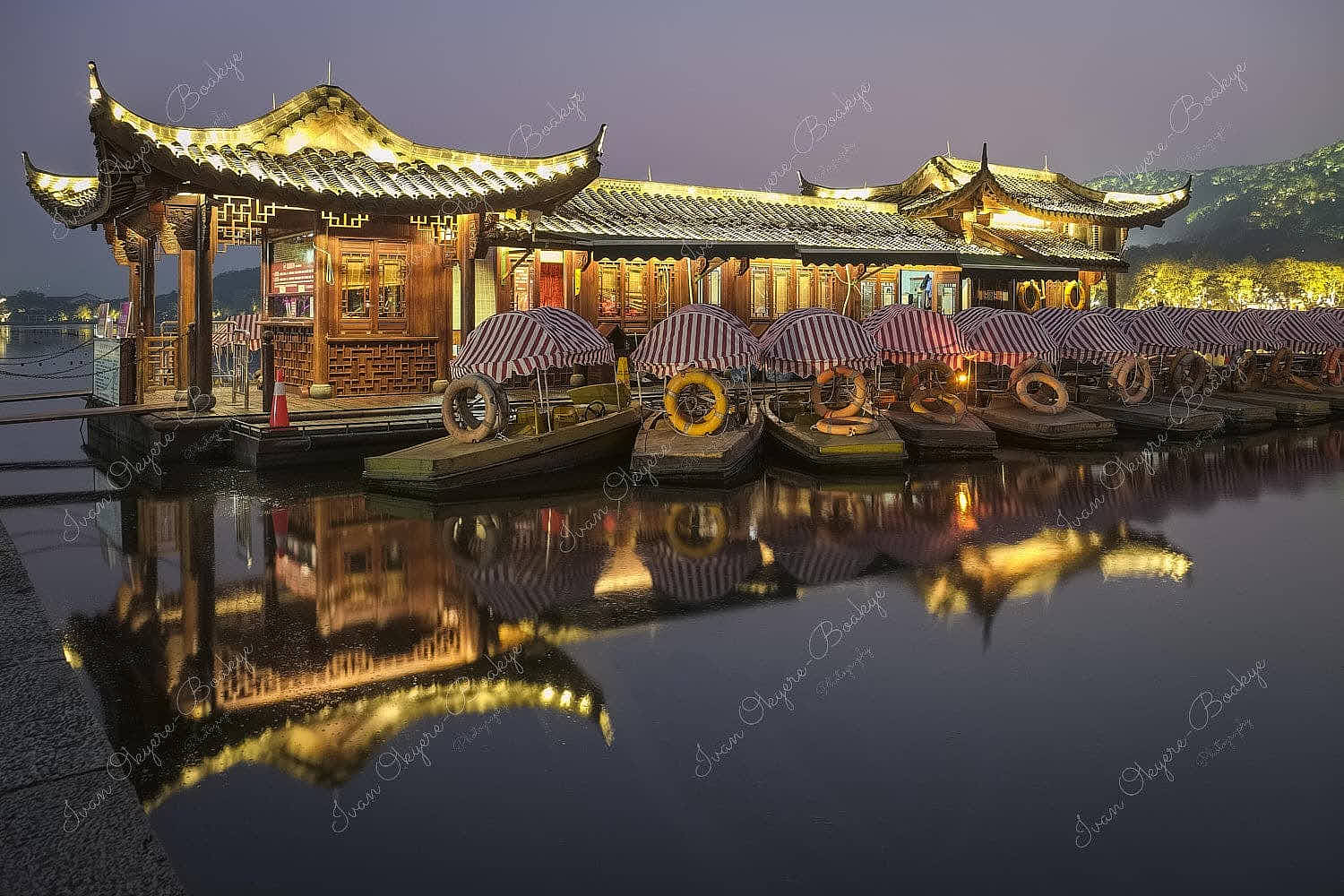 Moored boats at an illuminated Chinese design style pier in West Lake at night with reflections in the still water, Hangzhou, Zhejiang Province, China