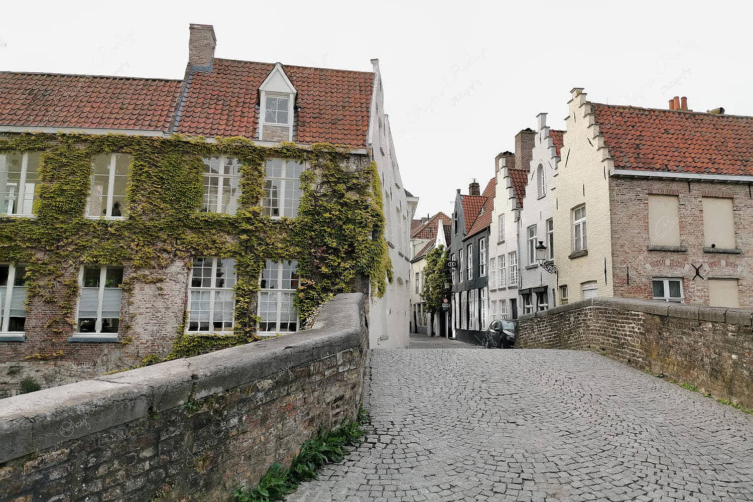 Classic view of a cobbled bridge leading into a side street surrounded by traditional crow- stepped gable styled houses in Groenerei, Bruges, Belgium